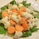 Chicken cauliflower salad served on a bed of spinach leaves.