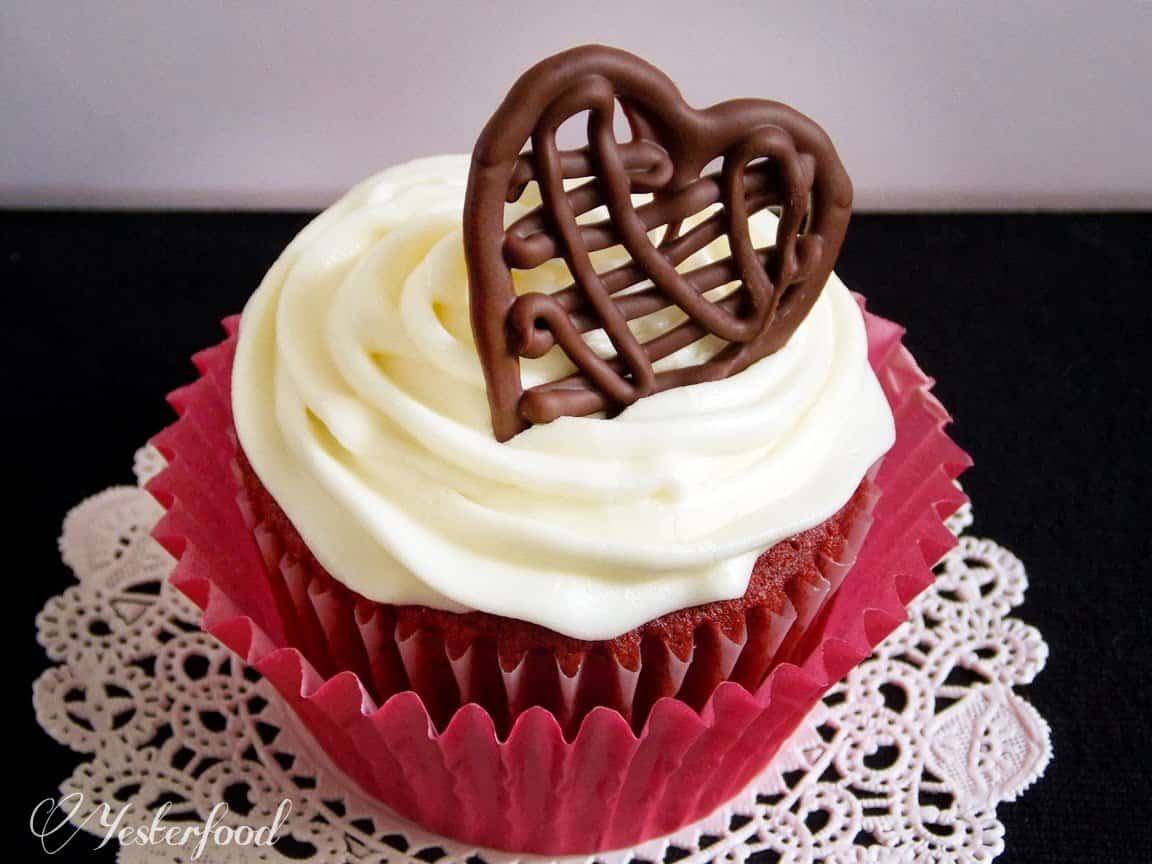 Chocolate drizzle heart garnishing a beautiful and delicious looking red velvet cupcake