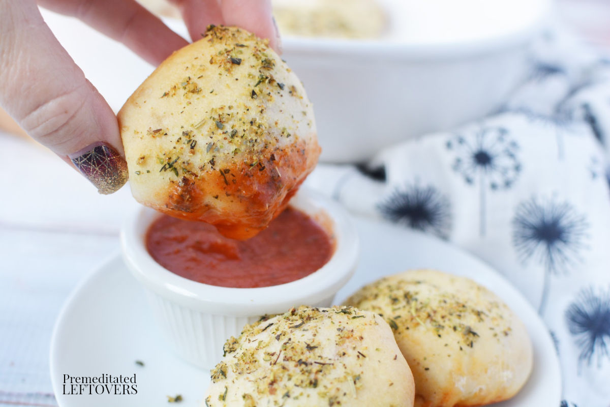 Dipping homemade pizza poppers in pizza sauce.