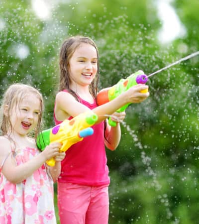 little girls playing with water guns on hot summer day. Cute children having fun with water outdoors.