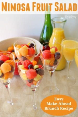 Mimosa Fruit Salad recipe in Wine glasses with mimosas on the side.