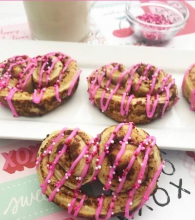 Valentine's Day Heart-Shaped Cinnamon Rolls with pink icing and Valentine Nonpareils on a white platter.