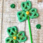 Shamrock pretzel pops covered in green candy melts with gold sprinkles