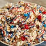 This patriotic candy-coated popcorn recipe is drizzled with red, white, and blue candy melts and topped with red and blue M&Ms.