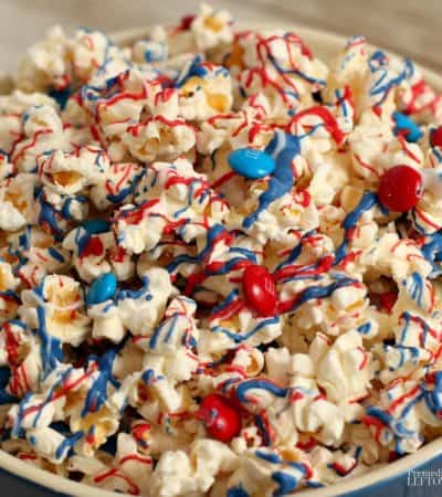 This patriotic candy-coated popcorn recipe is drizzled with red, white, and blue candy melts and topped with red and blue M&Ms.