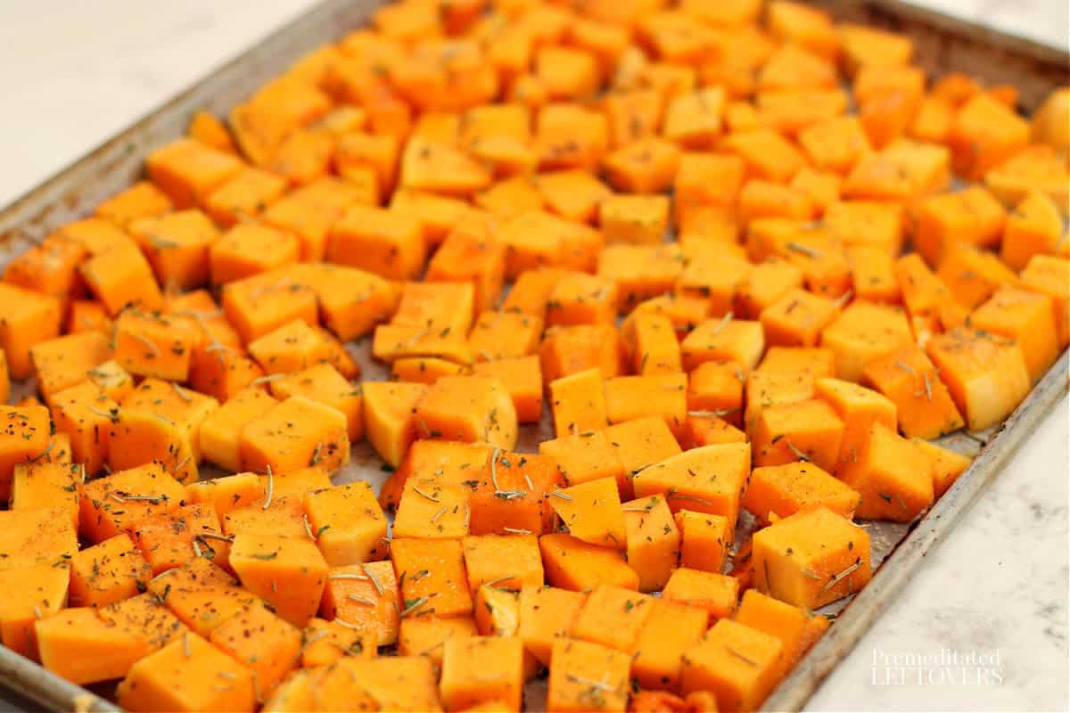 cubed sweet potatoes on baking tray coated with oil, rosemary, garlic, and onion