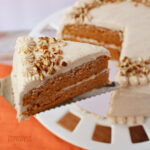a slice of homemade carrot cake topped with cinnamon cream cheese frosting and chopped pecans