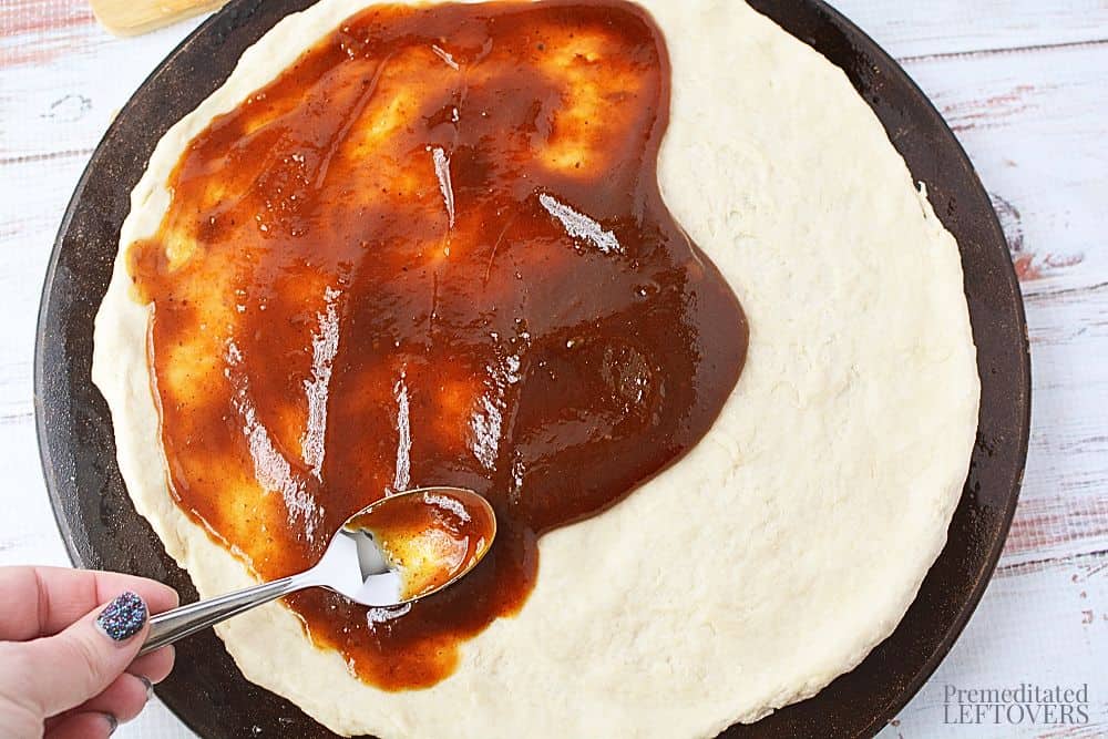 Spreading barbecue sauce on the pizza dough.