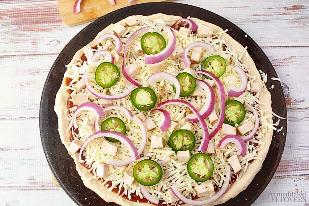 Cooked chicken cubes, red onions, and jalapenos on top of the shredded cheese, and the Chicken Barbecue Pizza is ready for the oven.